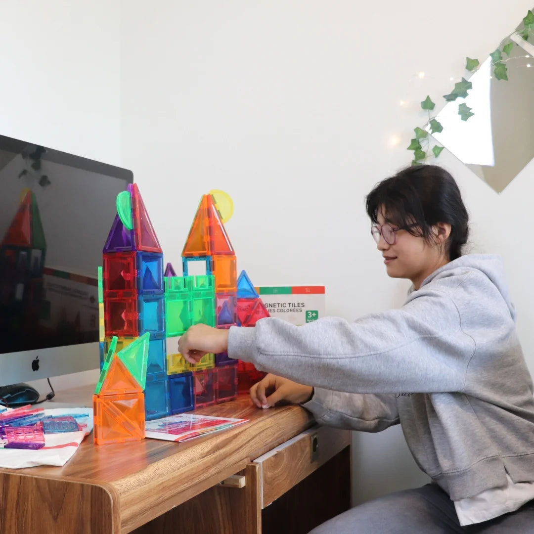Child building a colorful castle with Tessella Master Set – 106 Piece Magnetic Tiles on a desk, STEM educational toy for kids ages 3+, compatible with Connetix, PicassoTiles, Magna-Tiles.