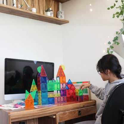 Child building a large colorful castle with Tessella Master Set – 106 Piece Magnetic Tiles on a desk, STEM educational toy for kids ages 3+, compatible with Connetix, PicassoTiles, Magna-Tiles.